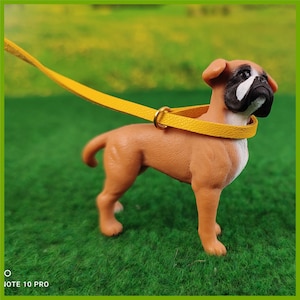 Ein Schleich Boxer mit einem gelben Halsband mit Leine