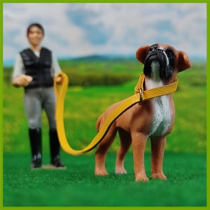 Ein Schleich Hund mit einem gelben Halsband mit Leine. Eine Schleich Figur führt den Hund.