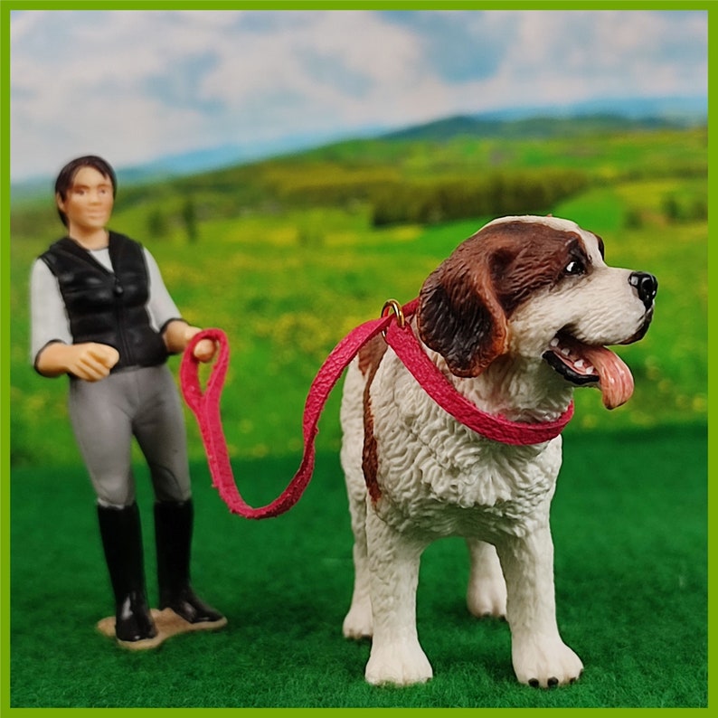 Ein Schleich Hund mit Halsband mit Leine in Pink. Eine Schleich Figur führt den Hund.