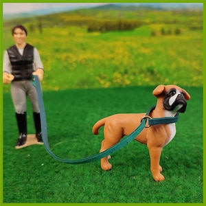 Ein Schleich Hund mit einem Halsband mit Leine in Türkis. Eine Schleich Figur führt den Hund.