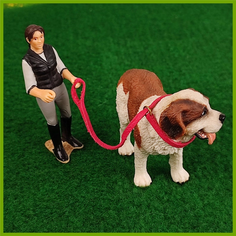 Ein Schleich Hund mit einem Halsband mit Leine in Pink. Eine Schleich Figur führt den Hund.