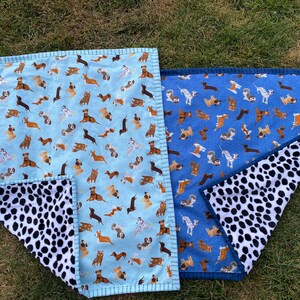 May include: Two dog-themed blankets. One is light blue with various dog breeds, the other is blue with similar dog illustrations. Both have a black and white dalmatian-spotted underside. The blankets are rectangular with a stitched border.