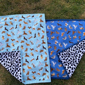 May include: Two dog-themed blankets. One is light blue with various dog breeds, the other is blue with similar dog illustrations. Both have a black and white dalmatian-spotted underside. The blankets are rectangular with a stitched border.