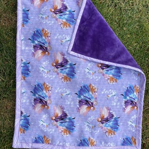May include: A baby blanket featuring a purple and white pattern with images of a princess and a snowman. The blanket has a soft, plush purple backing and a patterned border.