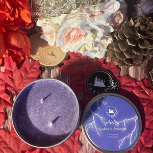 May include: A purple candle in a tin container with a label that reads "Aislin Leather & Lavender 8 oz - soy wax hand poured". The label has a lightning bolt design.