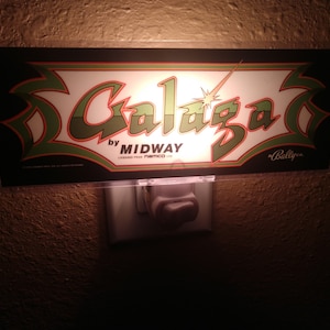 以下が含まれることがあります： 「Galaga by Midway Licensed from Namco Ltd. Ballyco.」と書かれた緑と白のナイトライト