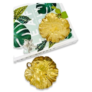 May include: Two gold leaf-shaped decorative trays with a textured surface. The trays have a small loop handle on the top.
