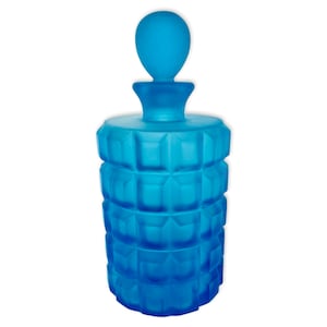 May include: A frosted blue glass bottle with a geometric design and a round stopper. The bottle is empty and has a vintage look.
