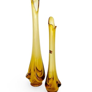 May include: A set of two amber glass vases with a unique, wavy design. The taller vase is approximately 12 inches tall and the shorter vase is approximately 8 inches tall.