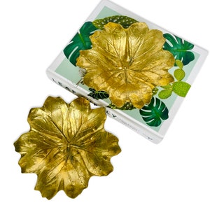Peut inclure: Deux bols décoratifs en forme de feuille dorée. Les bols sont en métal et ont une surface texturée. Les bols sont posés sur un livre avec une couverture verte et blanche.