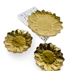 Pode incluir: Três bandejas de metal douradas com um design de flor. As bandejas são de tamanhos diferentes e estão empilhadas umas sobre as outras.