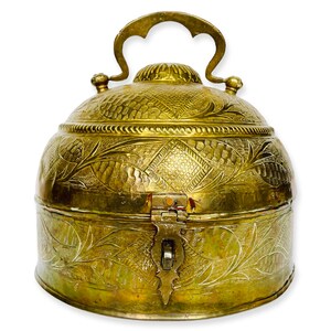 Può includere: Una scatola vintage in ottone con un design ornamentale e un coperchio incernierato. La scatola ha una maniglia sulla parte superiore e un chiavistello sul davanti.