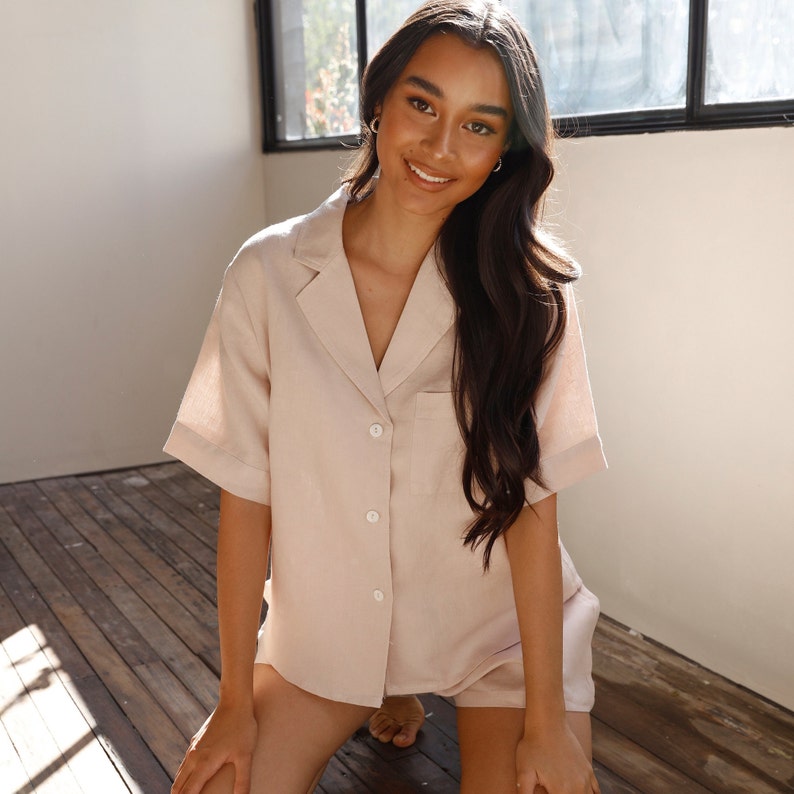 May include: A light beige linen pajama set with a collared shirt and shorts. The shirt has a button-up front and a chest pocket.