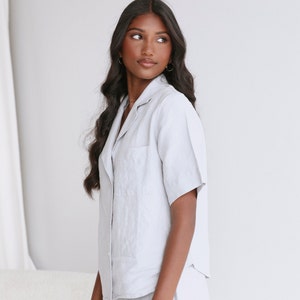 May include: A light gray linen shirt with a collared neckline and short sleeves. The shirt has a relaxed fit and a slightly oversized silhouette.