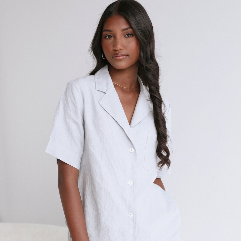 May include: A light blue linen shirt with a collared neckline, short sleeves, and a single button pocket on the left chest. The shirt has a relaxed fit and is button-up.