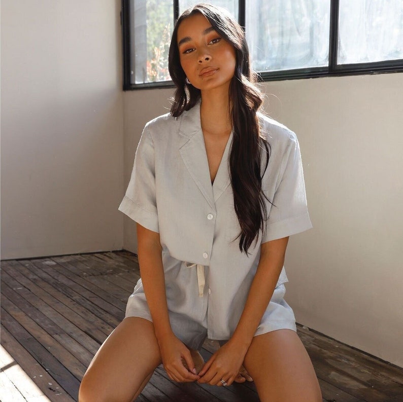 May include: A light blue linen pajama set with a collared shirt and shorts. The shirt has a button-up front and a drawstring waist. The shorts have a relaxed fit.