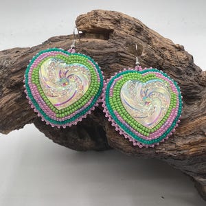May include: Heart-shaped dangle earrings featuring a central iridescent swirl cabochon surrounded by concentric rows of lime green, teal, and light pink seed beads. The earrings are finished with silver-toned metal hooks for attachment.