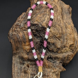 May include: A pink, black, and white beaded key chain with a silver key ring. The key chain is made of small beads and is about 15 inches long.