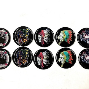 May include: A collection of ten black, round buttons with various designs. The designs include a bear claw, a Native American headdress, a skull with a headdress, and a wolf's head. The buttons have a glossy finish.