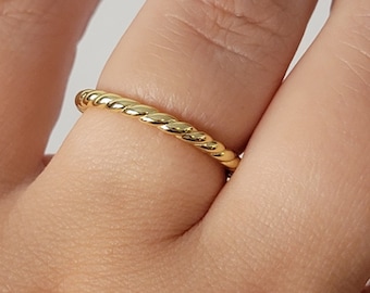 May include: A simple gold band ring with a twisted design.