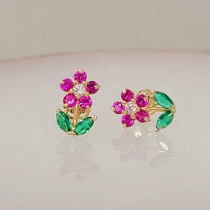 May include: A pair of gold flower earrings with pink and green gemstones. The earrings are small and delicate, and they would make a great gift for a special occasion.