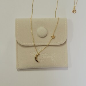 May include: A gold necklace with a crescent moon and star pendant. The necklace is in a white velvet pouch with the words "Jennifer Zeuner" printed on it.