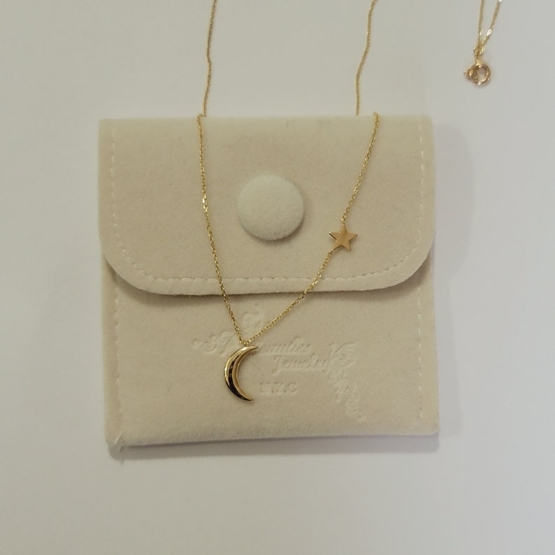May include: A gold necklace with a crescent moon and star pendant. The necklace is in a white velvet pouch with the words "Jennifer Zeuner" printed on it.