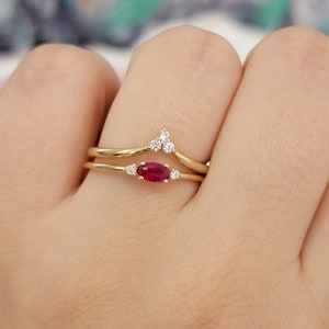 May include: A gold ring set with a ruby and small diamonds. The ring is on a finger.