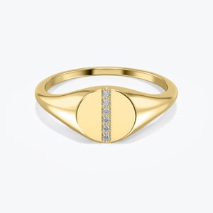 Op de afbeelding: Een gouden signet ring met een ronde, platte bovenkant met een verticale rij kleine diamanten.