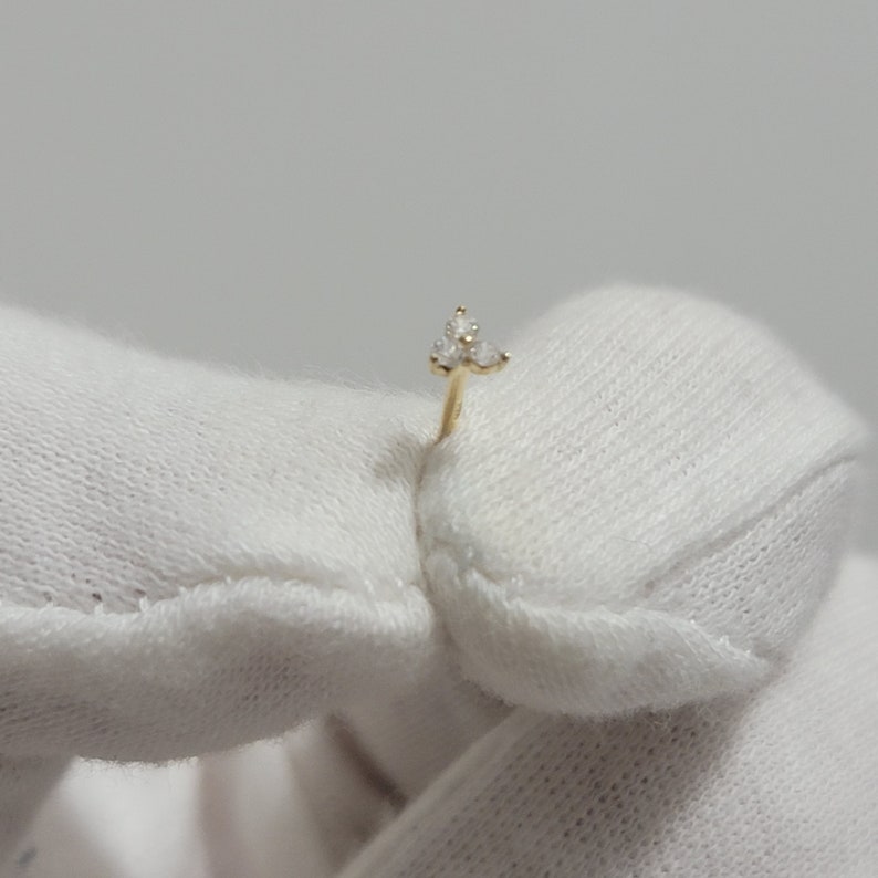 May include: A gold nose ring with three small clear stones set in a triangular shape.