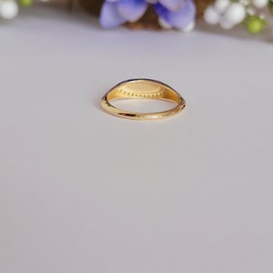 May include: A gold signet ring with a smooth, oval-shaped top. The ring has a delicate band and a row of small, evenly spaced dots around the top.