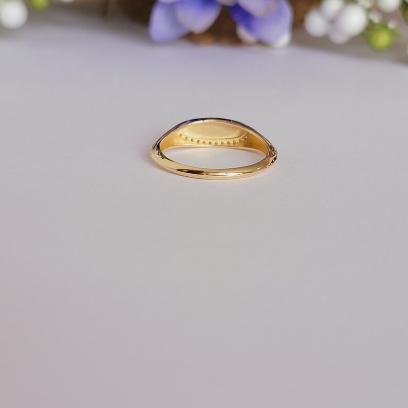 May include: A gold signet ring with a smooth, oval-shaped top. The ring has a delicate band and a row of small, evenly spaced dots around the top.