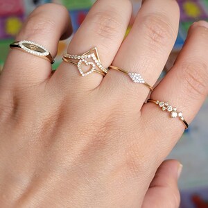 May include: A hand wearing four gold rings with small diamonds. The rings are stacked on two fingers. The rings are delicate and feminine.