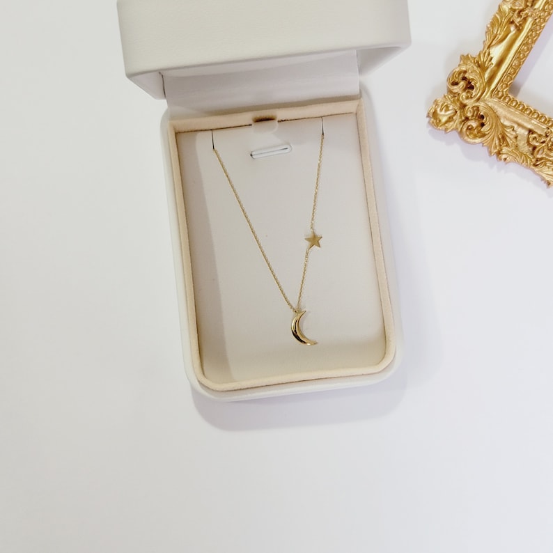 May include: A gold necklace with a crescent moon and star pendant in a white box.