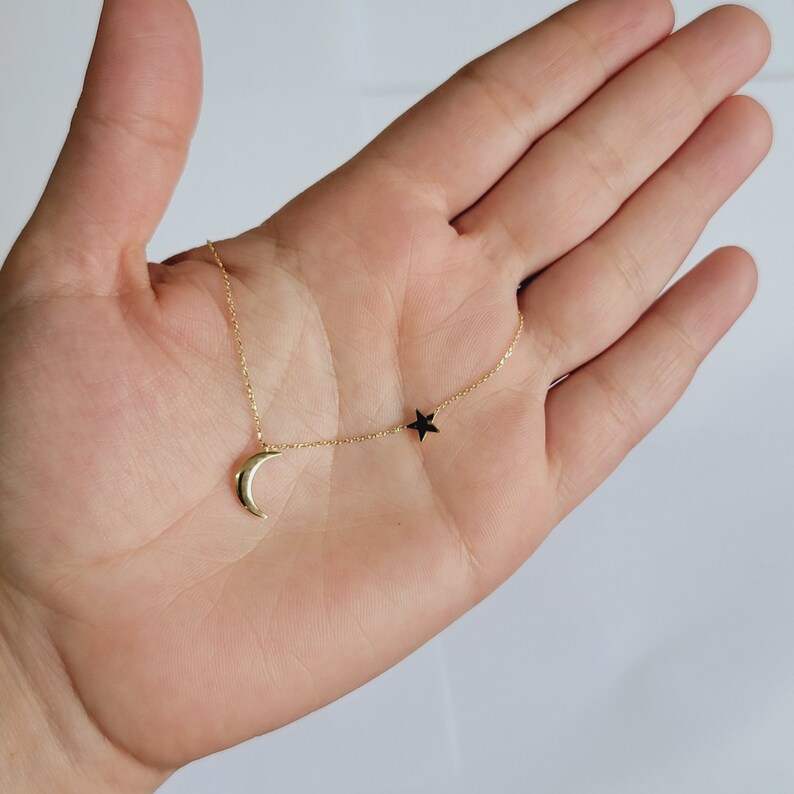 May include: A gold chain necklace with a crescent moon charm and a black star charm.