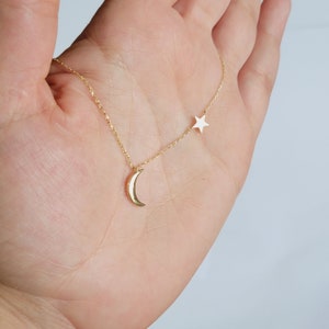 May include: A gold chain necklace with a crescent moon and a star pendant. The moon pendant is gold and the star pendant is white.