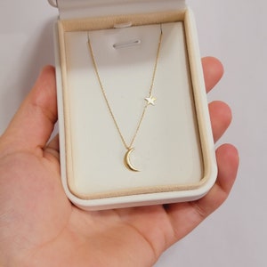 May include: A gold necklace with a crescent moon pendant and a small star charm. The necklace is displayed in a white box.