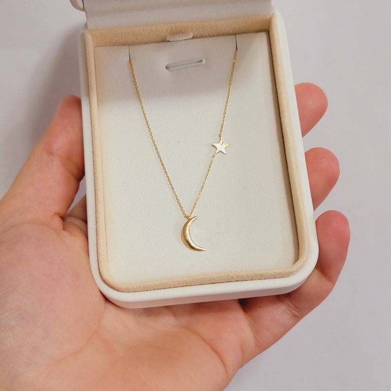 May include: A gold necklace with a crescent moon pendant and a small star charm. The necklace is displayed in a white box.