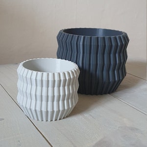 May include: Two geometric planters, one white and one grey, with a textured, ribbed design. The planters are made of a durable material and are perfect for adding a modern touch to any home.