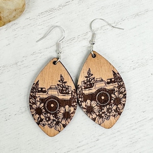 May include: A pair of wooden earrings with a teardrop shape. Each earring features a laser-engraved design of a vintage camera with flowers surrounding it.
