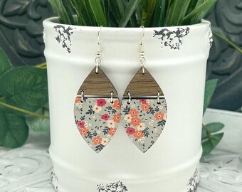 May include: A pair of teardrop-shaped earrings featuring a dark brown wood top section and a light gray bottom section with a floral pattern in shades of red, orange, and white. The earrings hang from silver-toned metal hooks and jump rings.