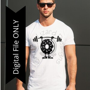 May include: A white t-shirt with a black graphic of a donut lifting weights. The donut has a white frosting and sprinkles. The text "Craft Wizard Designs" is printed on the shirt.