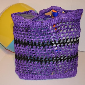 May include: Purple and black crocheted tote bag with a beach ball and towel inside.