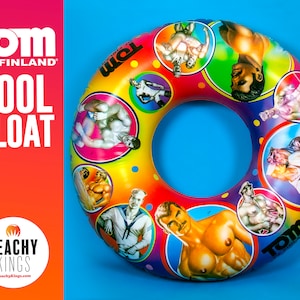 Può includere: Un galleggiante per piscina gonfiabile colorato a forma di anello. Il galleggiante è decorato con immagini di uomini in varie pose, tra cui un marinaio, un lottatore e un uomo con i baffi. Il galleggiante è stampato con il testo "Tom of Finland" e "Peachy Kings".