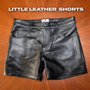 May include: Black leather shorts with a button closure, belt loops, and front pockets. The shorts have a classic design and are made of a smooth, shiny leather material. The text "LITTLE LEATHER SHORTS" is displayed at the top.