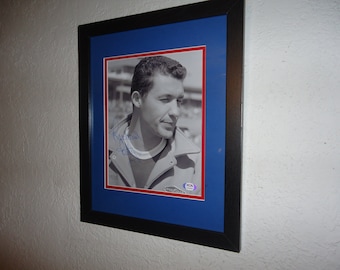 May include: A black and white photograph of a man wearing a jacket, signed with a blue signature. The photo is framed in a black frame with a blue mount. The photo is authenticated with a PSA/DNA hologram sticker.