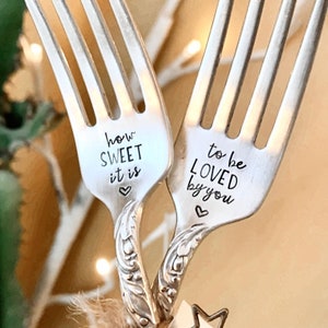 Può includere: Due forchette d'argento con le scritte "how SWEET it is" e "to be LOVED by you", ognuna con un cuore. Sono legate con spago e un ciondolo a forma di stella, perfette per un regalo.