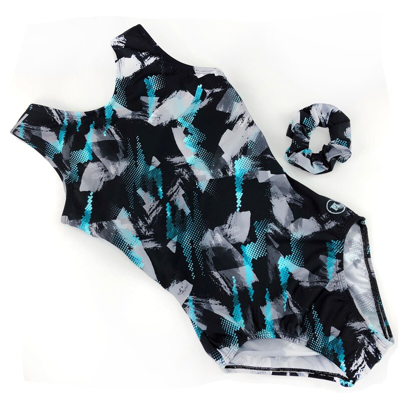 May include: Black leotard with a blue and grey abstract print. The leotard has a scoop neck and a racerback. It comes with a matching blue scrunchie.