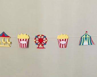 May include: A colourful paper garland featuring carnival-themed cut-outs, including a carousel, popcorn buckets, a Ferris wheel, a tent, and tickets. The garland is strung on a white string and is ideal for a party or celebration.