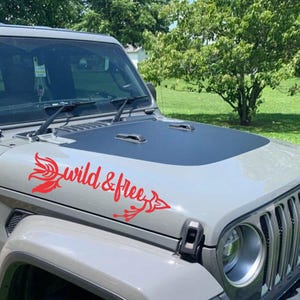 May include: A red vinyl decal with a stylized arrow and the text "wild & free" on a gray Jeep.